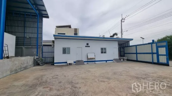 Warehouse for rent in Phra Samut Chedi, Samut Prakan - Single-storey office and staff quarters beside a wide gate and paved forecourt.