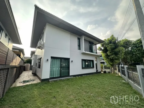 บ้าน ให้เช่าหรือขายในLam Luk Ka, Pathum Thani - มุมด้านข้างของบ้านพร้อมสนามหญ้า ประตูบานเลื่อนกระจก และรั้วรอบโครงการ มีต้นไม้ให้ร่มเงา