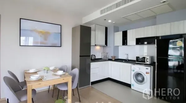 Condominium for rent or sale in Watthana, Bangkok - Modern white U-shaped kitchen with refrigerator, microwave and in-unit washing machine beside a dining nook.