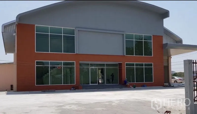 Factory for rent or sale in Mueang Samut Prakan, Samut Prakan - Modern factory exterior with large glass facade and a spacious forecourt.