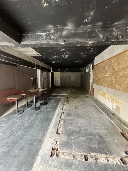 零售空间 出租在Watthana, Bangkok - 狭长开间商铺，黑色裸顶，地面有管线沟槽并摆放少量圆桌。