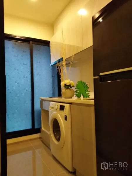 Condominium for rent in Huai Khwang, Bangkok - Compact kitchenette with washing machine, upper cabinets and fridge by a frosted window