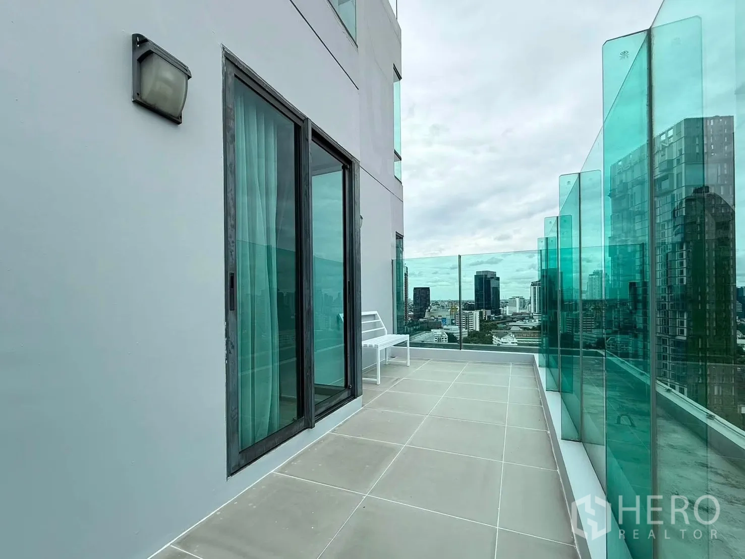 Condominium for rent in Khlong Toei, Bangkok - Spacious terrace with glass balustrade and skyline view beside sliding glass doors.