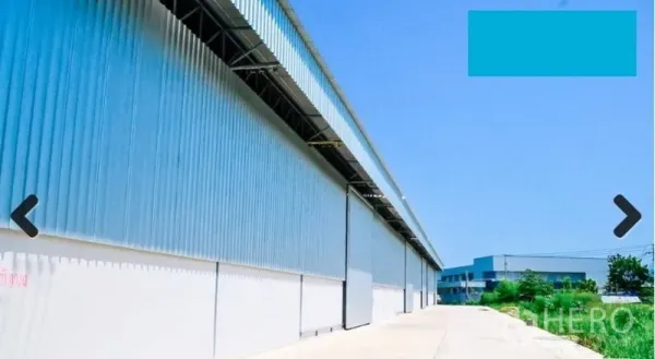 Warehouse for rent in Bang Phli, Samut Prakan - Side view of industrial warehouse facade showing loading access along a paved road and green verge.