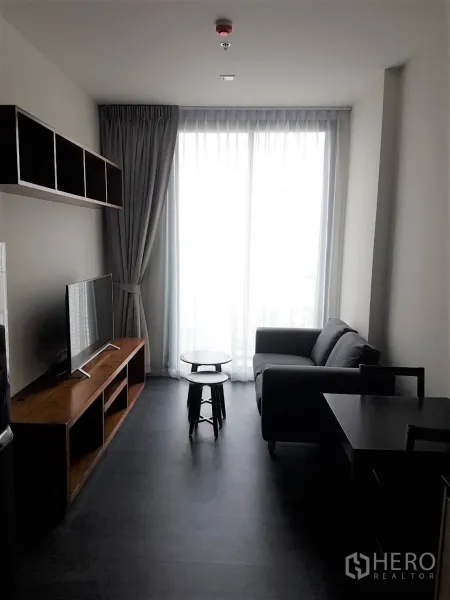 Condominium for rent or sale in Watthana, Bangkok - Bright living room with sofa, TV console and floor-to-ceiling window with sheer curtains in a Sukhumvit condo.