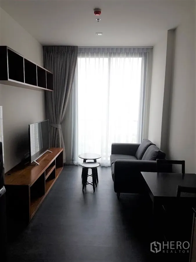 Condominium for rent or sale in Watthana, Bangkok - Bright living room with sofa, TV console and floor-to-ceiling window with sheer curtains in a Sukhumvit condo.