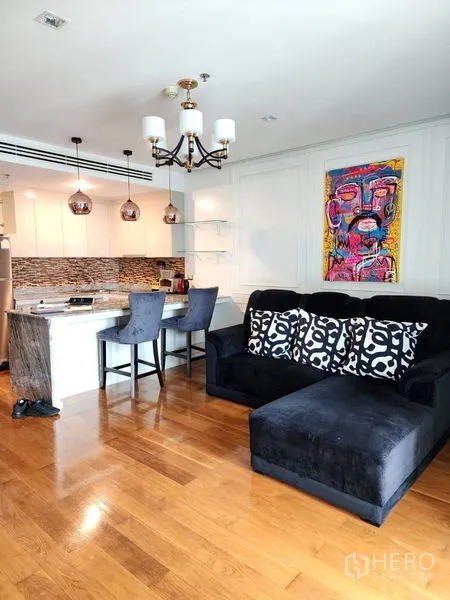 公寓 出租在Bang Rak, Bangkok - 开放式客厅与黑色转角沙发、石材中岛、吊灯、木地板及彩色墙面艺术品。