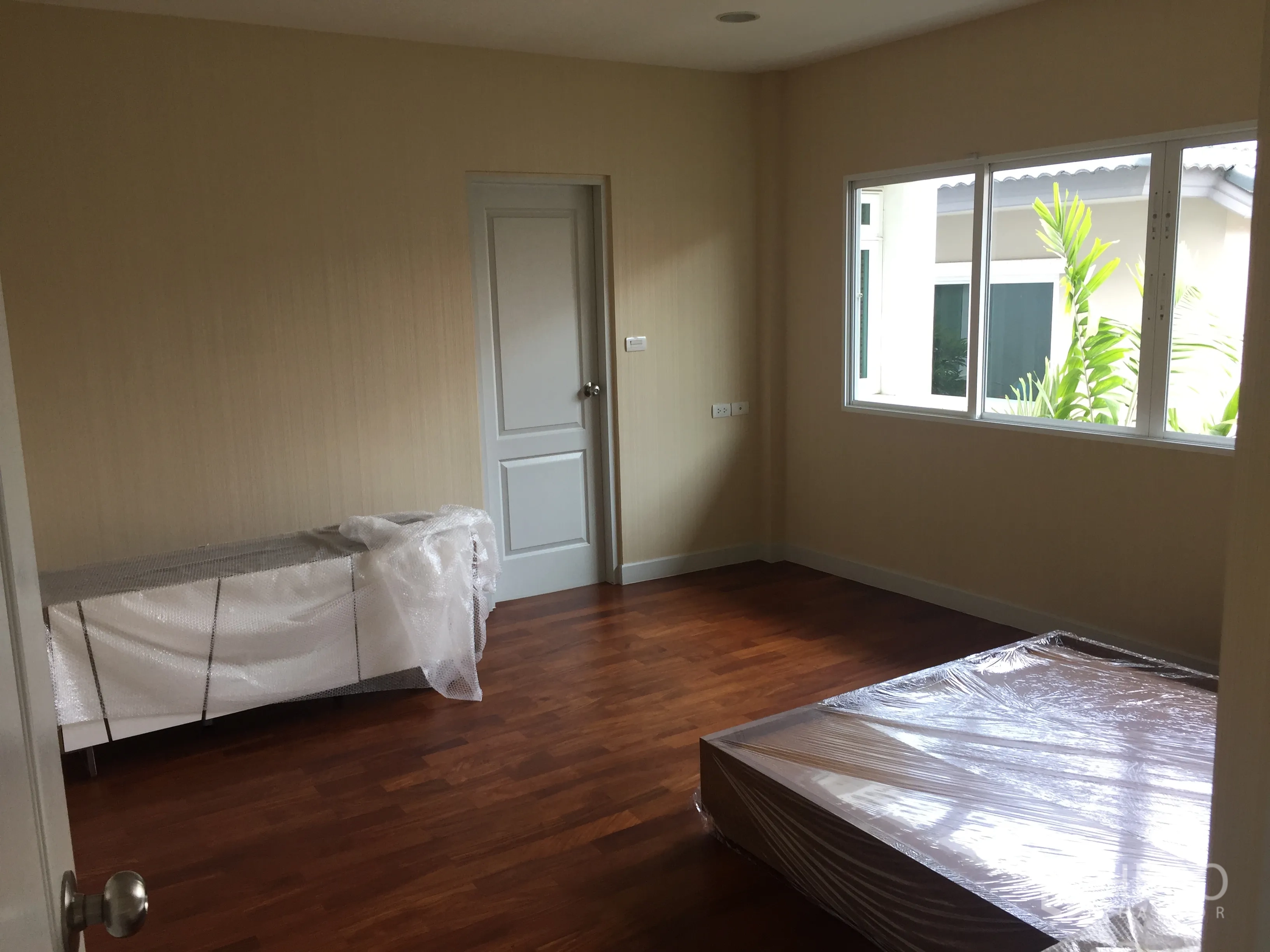 Detached House for sale in Saphan Sung, Bangkok - Bedroom with large window and partially wrapped furniture ready to move in.