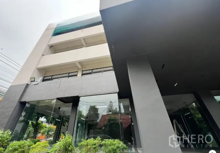 零售空间 出租在Suan Luang, Bangkok - 现代零售建筑，深色石材立面与立柱，整面落地玻璃，周围绿化。