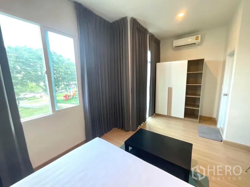 Townhouse for rent in Bang Phli, Samut Prakan - Corner master bedroom with tall curtains, wide windows and wardrobe overlooking greenery.