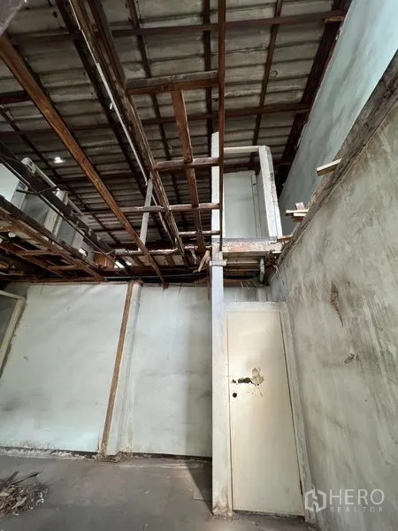 Shophouse for rent or sale in Bang Khen, Bangkok - Close view of exposed ceiling frames and a worn white door inside the building.