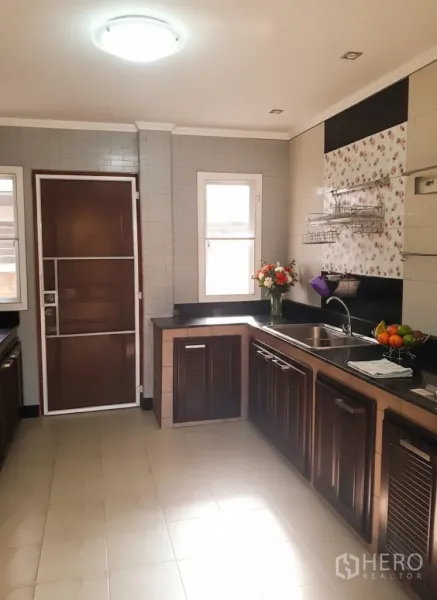 บ้าน ให้เช่าในLat Krabang, Bangkok - ห้องครัวรูปตัวแอลสว่าง เคาน์เตอร์หินแกรนิต ตู้ไม้สีน้ำตาล อ่างล้างจาน และประตูหลังมีช่องหน้าต่าง