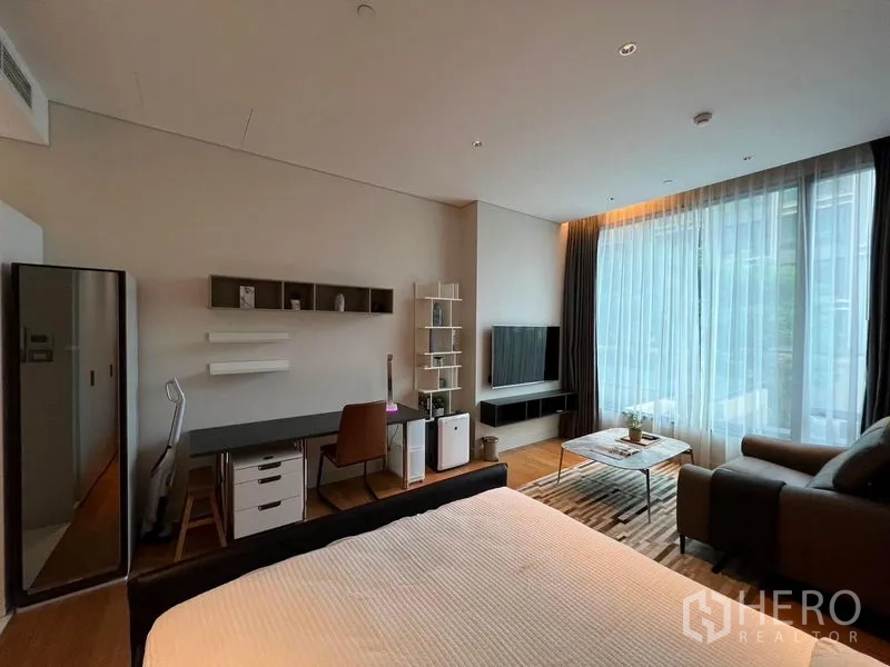 Condominium for rent in Pathum Wan, Bangkok - Bright 40 sqm studio condo with bed, work desk, sofa, TV wall, wood floors and floor‑to‑ceiling windows with sheer curtains