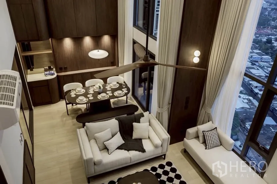 Condominium for rent in Khlong Toei, Bangkok - Aerial view from mezzanine of living and dining area with ceiling fan and tall windows.