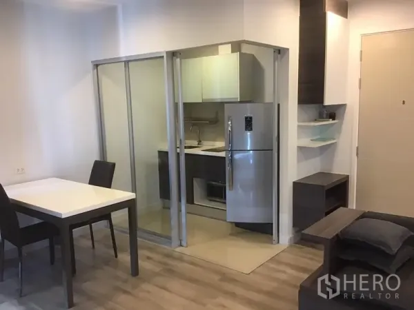 Condominium for rent in Sathon, Bangkok - Compact fitted kitchen behind sliding glass doors with stainless refrigerator next to a dining table.