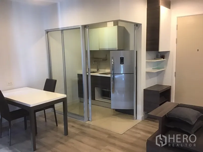 Condominium for rent in Sathon, Bangkok - Compact fitted kitchen behind sliding glass doors with stainless refrigerator next to a dining table.