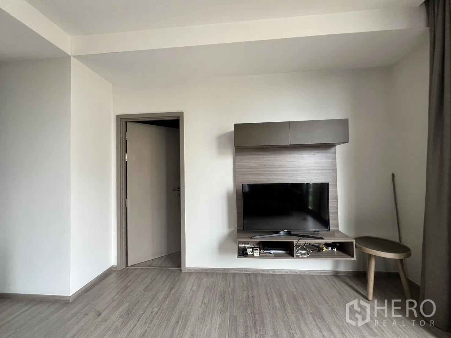 Condominium for rent in Watthana, Bangkok - TV mounted on a wood feature wall with floating shelf and a small side table.