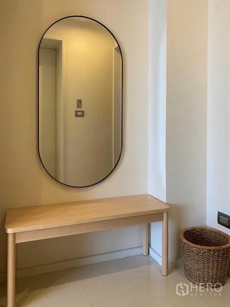 Condominium for rent in Sathon, Bangkok - Entry hallway with oval mirror, light wood bench and wicker basket.