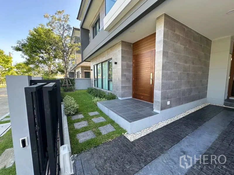 บ้าน ให้เช่าในBang Phli, Samut Prakan - เฉลียงหน้าบ้าน ประตูไม้กรอบใหญ่ ผนังลายหิน และสนามหญ้าเล็ก