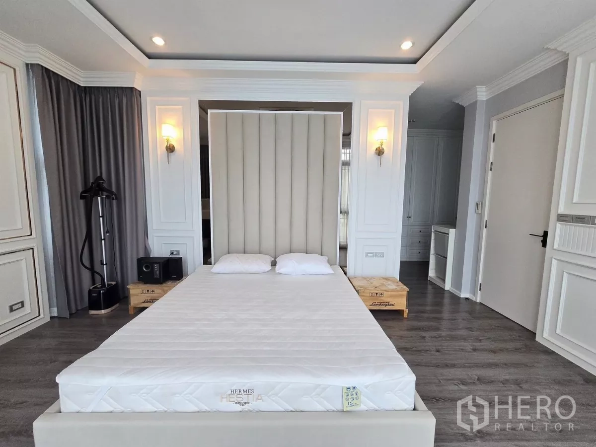Detached House for rent in Prawet, Bangkok - Primary bedroom with tall padded headboard, wood floors and soft wall sconces.