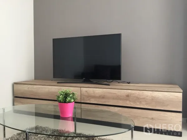 Condominium for rent in Pathum Wan, Bangkok - Close-up of wood TV cabinet with flat-screen television and a glass coffee table holding a pink planter.