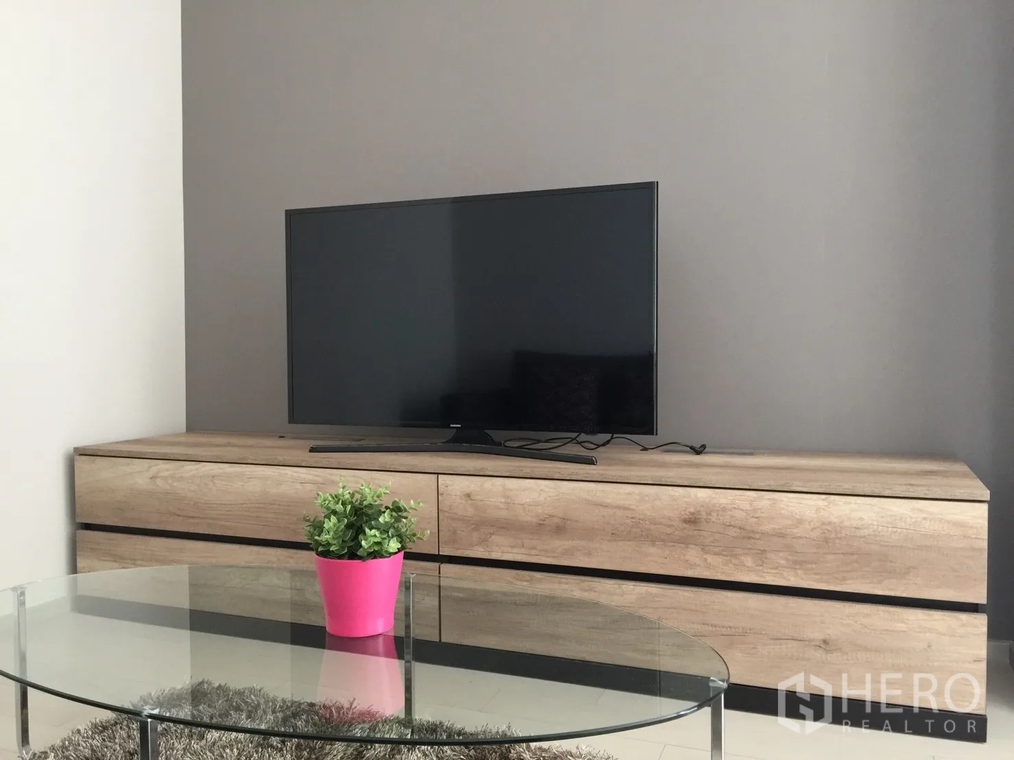 Condominium for rent in Pathum Wan, Bangkok - Close-up of wood TV cabinet with flat-screen television and a glass coffee table holding a pink planter.