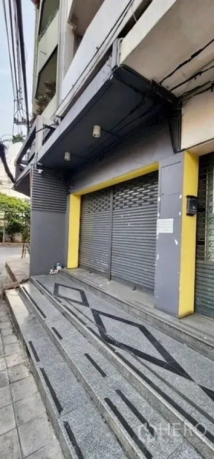 สำนักงานที่บ้าน ให้เช่าในSathon, Bangkok - ด้านหน้าอาคารสไตล์ตึกแถว ประตูม้วนสีเทา เสาเหลือง และบันไดพื้นลายหินขัดติดถนน