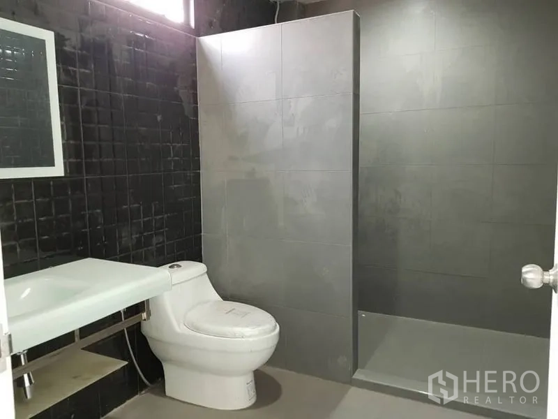 Home Office for rent or sale in Khlong Toei, Bangkok - Modern bathroom with walk‑in shower, gray tiles, and a sleek counter basin.