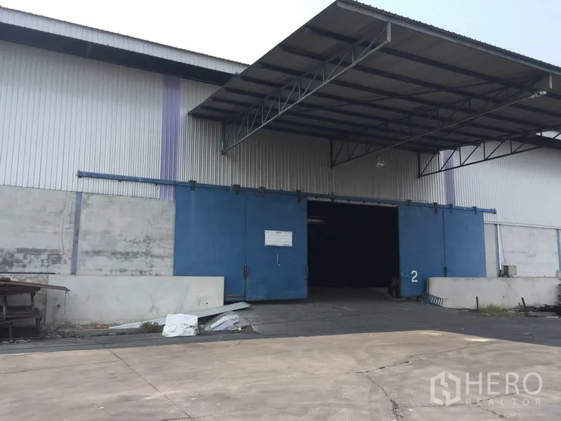 Warehouse for rent in Pathum Thani - Warehouse exterior with large blue sliding doors and a covered loading bay.