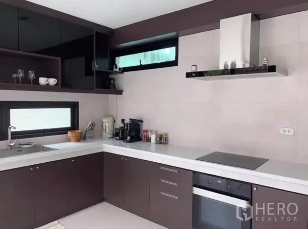 Townhouse for rent in Din Daeng, Bangkok - Close-up of L-shaped kitchen with built-in oven, cooktop, upper cabinets and slim windows.