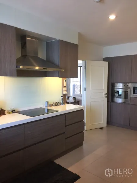 Condominium for rent in Watthana, Bangkok - Modern enclosed kitchen with induction cooktop, range hood and sleek wood cabinetry.