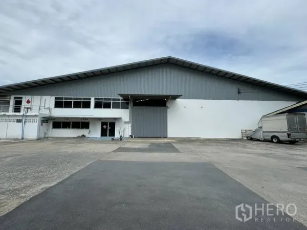 货栈 出租在Mueang Pathum Thani, Pathum Thani - 仓库正面广角，配大型卷闸门和宽敞硬化卡车场地。