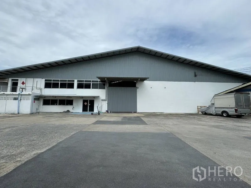 货栈 出租在Mueang Pathum Thani, Pathum Thani - 仓库正面广角，配大型卷闸门和宽敞硬化卡车场地。