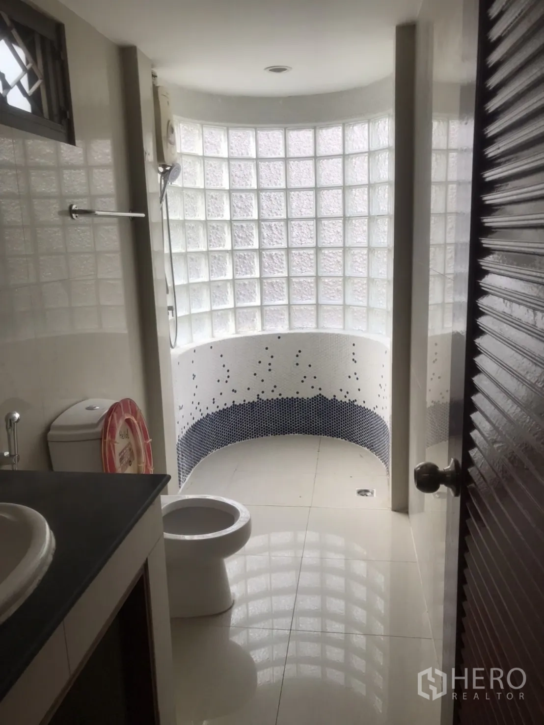 Home Office for rent in Khlong Toei, Bangkok - Modern bathroom featuring a curved glass-block wall, shower area, and a vanity counter.