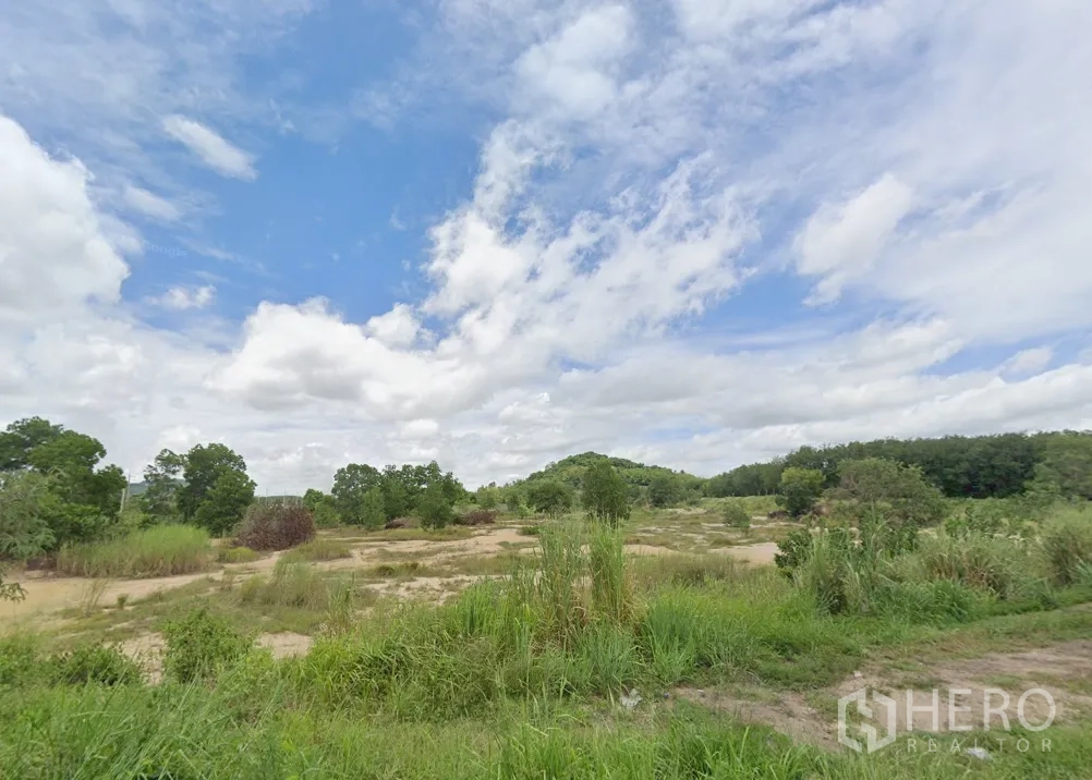 Land for sale in Si Racha, Chon Buri - Expansive Bo Win land parcel with natural grass, scattered trees and low hills under a bright cloudy sky.