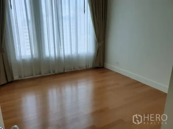 Condominium for rent in Watthana, Bangkok - Cozy bedroom with large curtained window and polished wooden floors in a minimalist condominium.