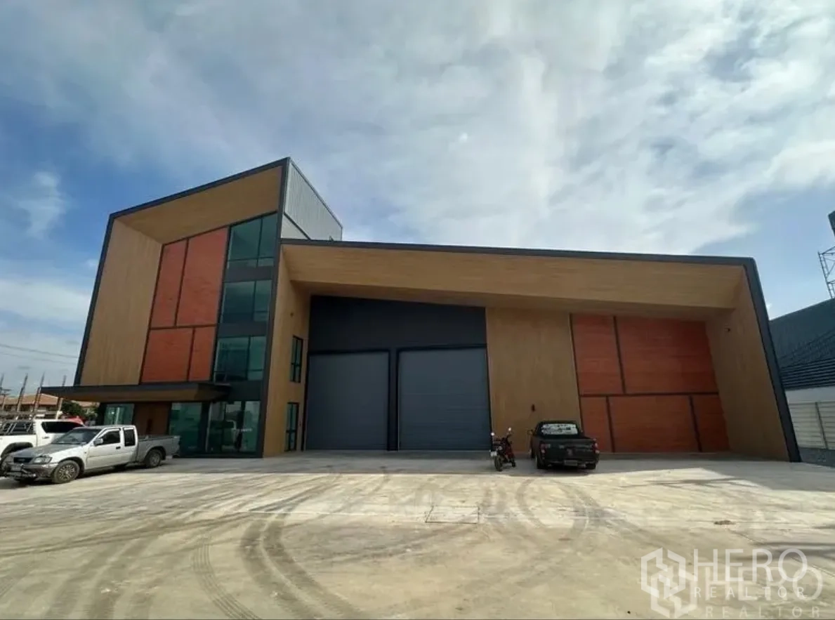 โกดัง for sale in Lam Luk Ka, Pathum Thani - ด้านหน้าตัวอาคารร่วมสมัย ประตูม้วนคู่สีเทา และลานคอนกรีตกว้าง