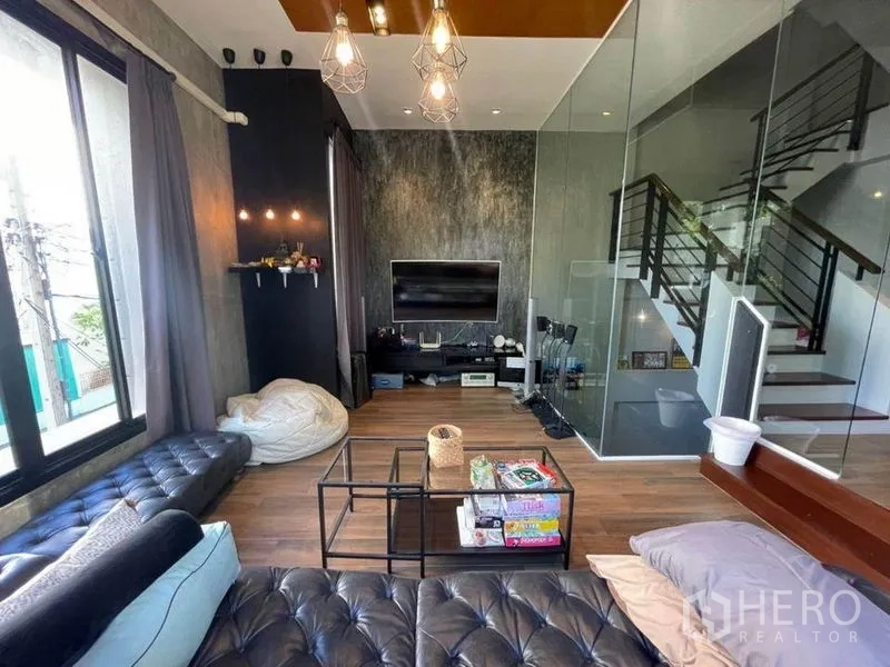 ทาวน์เฮาส์ ขายในBang Phli, Samut Prakan - ห้องนั่งเล่นอบอุ่น ผนังทีวี กั้นกระจก เห็นบันได และโซฟาหนัง.