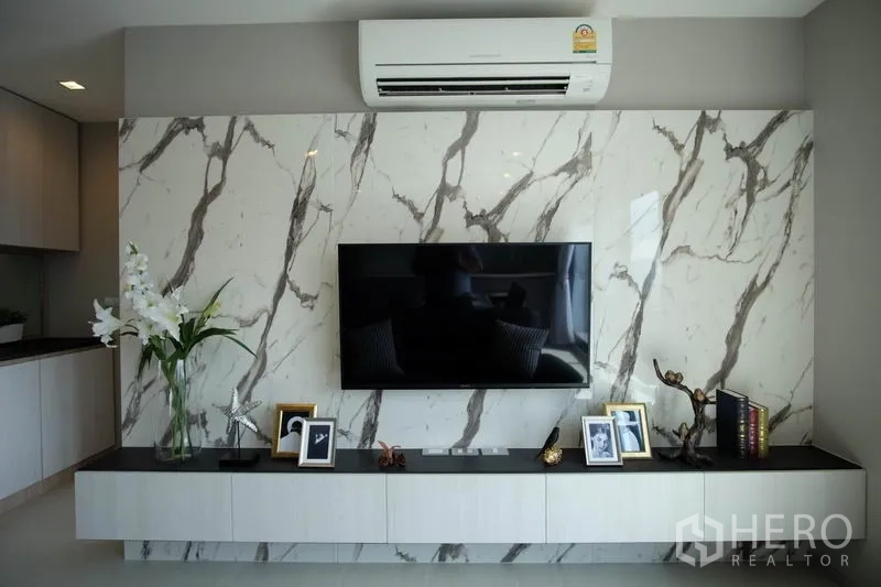 Condominium for rent in Khlong Toei, Bangkok - Marble-clad TV wall with floating cabinet, decor accents and air conditioner above.