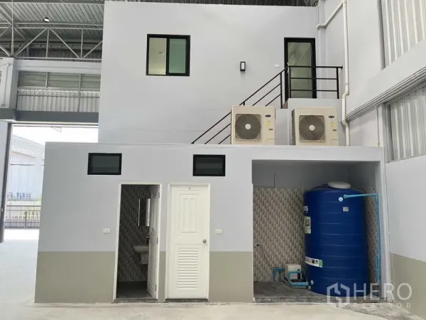 Warehouse for rent in Khlong Luang, Pathum Thani - Warehouse utility zone with restroom, storage room and blue water tank beneath the mezzanine.