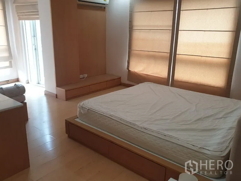Condominium for rent in Watthana, Bangkok - Bright master bedroom with platform bed, built-in storage, and floor-to-ceiling windows.