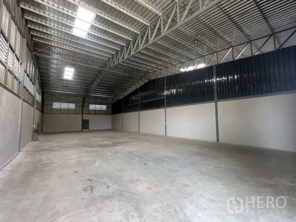 Warehouse for rent in Bang Bua Thong, Nonthaburi - Spacious warehouse interior with high steel truss roof, skylights and concrete flooring.
