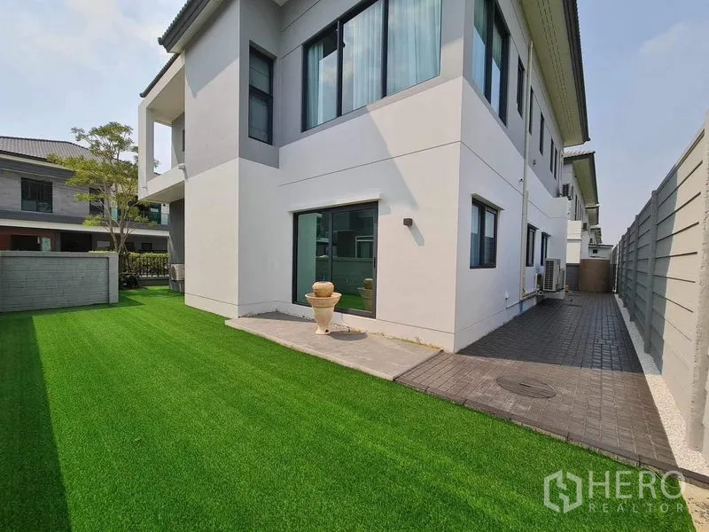 Detached House for rent or sale in Bang Phli, Samut Prakan - Backyard with wide green lawn, sliding door and paved path.