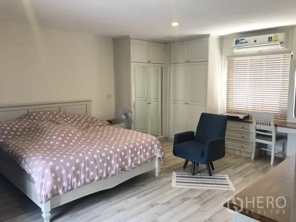 Townhouse for rent or sale in Saphan Sung, Bangkok - Master bedroom with king bed, built-in wardrobes, wood-style flooring, and a study corner.