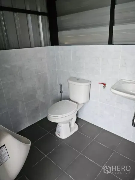 Warehouse for rent in Wang Thonglang, Bangkok - Clean tiled restroom inside the warehouse with toilet and wall-mounted sink.