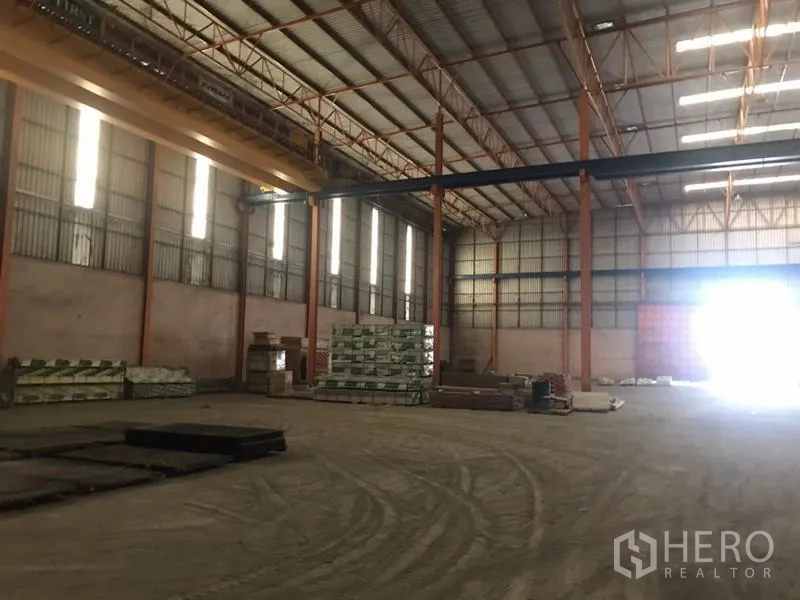 Home Office for sale in Khlong Luang, Pathum Thani - Open warehouse floor with materials and tall vertical windows admitting daylight.