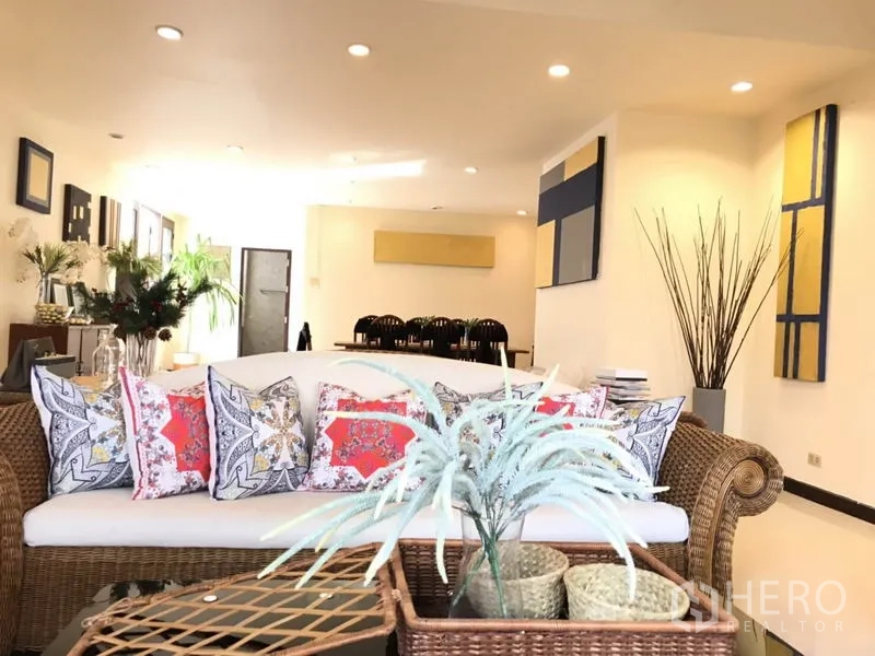 บ้าน ให้เช่าในPhra Khanong, Bangkok - ห้องนั่งเล่นและรับประทานอาหารแบบเปิด โซฟาหวาย ต้นไม้ และงานศิลป์สมัยใหม่