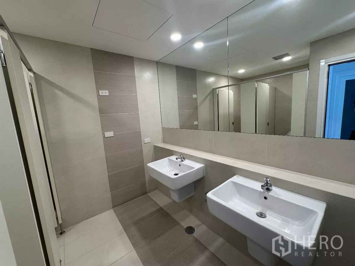 Office Space for rent in Watthana, Bangkok - Modern restroom featuring two wall-mounted sinks, large mirror, neutral tiles, and private stalls.