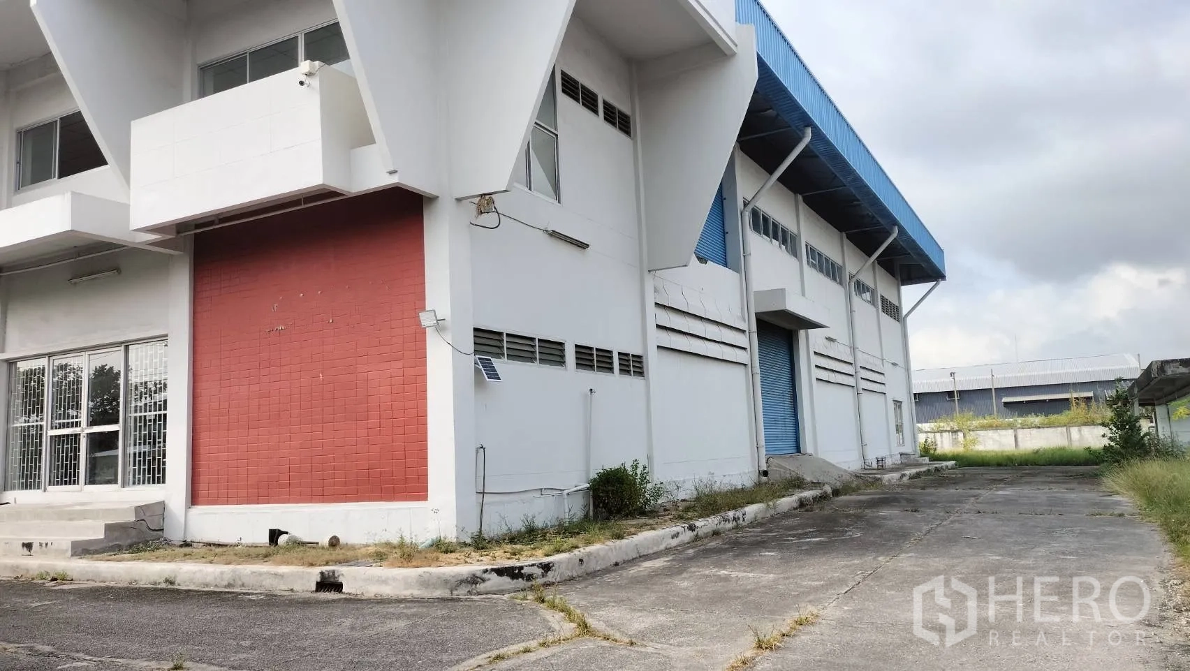 Factory for rent in Lat Krabang, Bangkok - Exterior of white factory with red accent wall, windows, and a loading ramp beside a wide driveway.