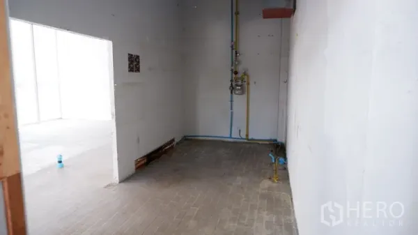 零售空间 出租在Watthana, Bangkok - 后勤区带管线与白色墙面，通向主营业空间的门洞。